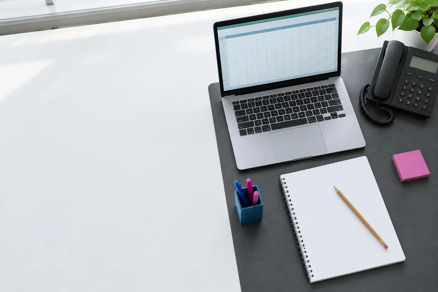 Symbolbild: Laptop mit Tabelle, Notizbuch und Telefon auf einem Arbeitsplatz